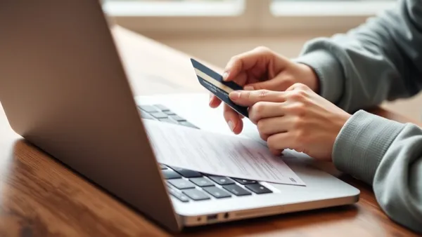 Pessoa pagando contas pelo notebook com cartão de crédito na mão, representando o pagamento de boletos no cartão para acumular milhas