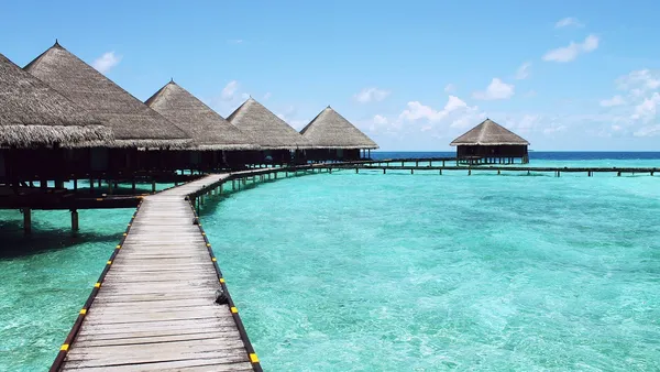 Bangalôs sobre a água em resort tropical com piscina e mar azul-turquesa